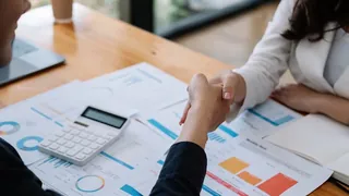 Pessoas apertando as mãos, apoiado sobre a mesa que contem calucadora e documentos relatorios financeiro sinalizando um acordo